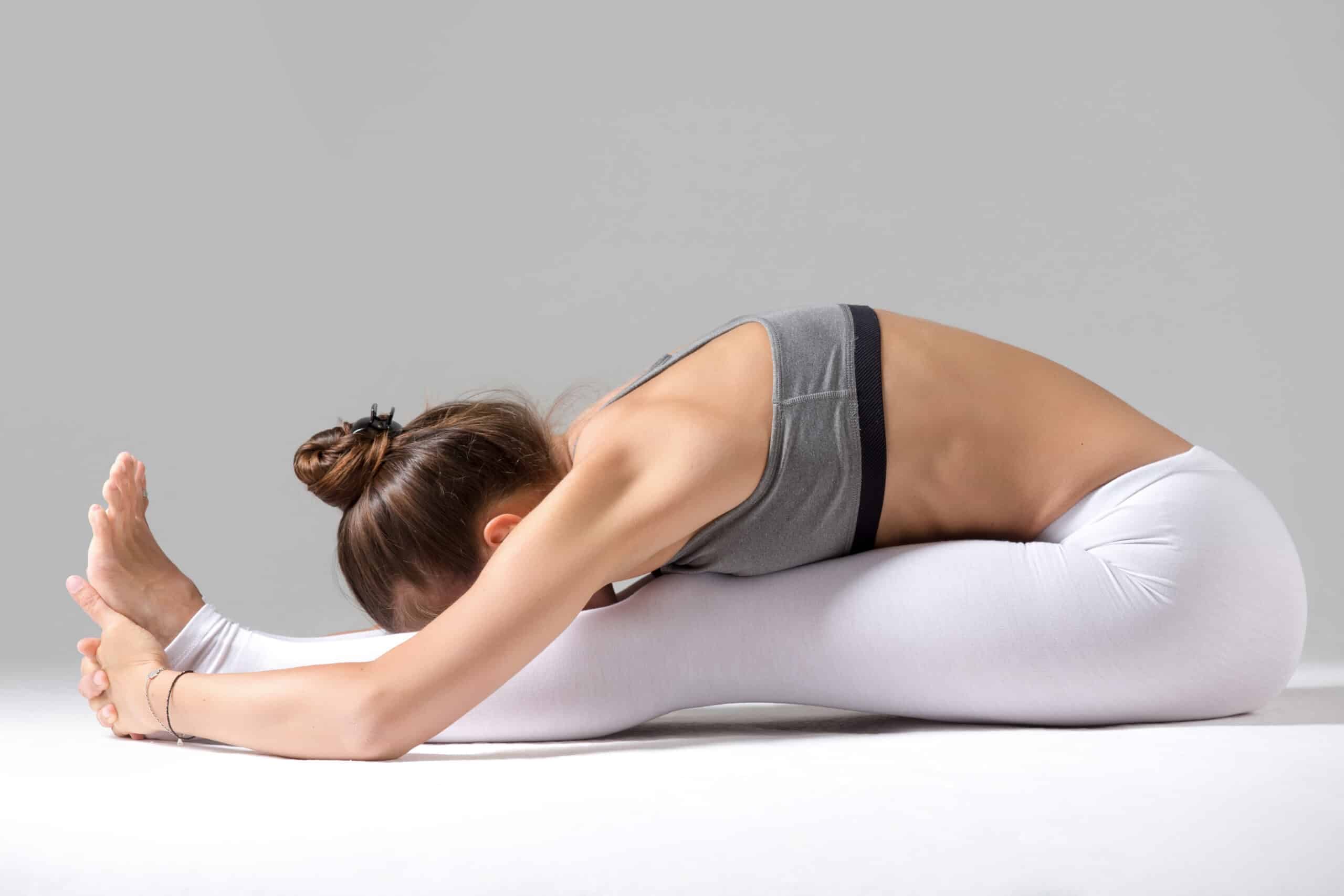 Young woman in paschimottanasana pose, grey studio background Seated Forward Bend scaled